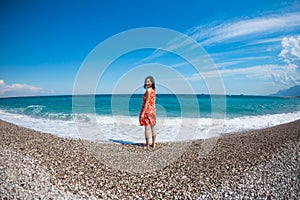 A girl in a dress walks along the beach and looks at the sea