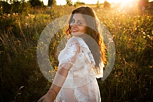 Girl in a dress walks in the field at sunset