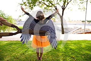 A girl dressed as a witch with an orange skirt and black wings. The girl is seen with her back turned and pruning shears are seen photo