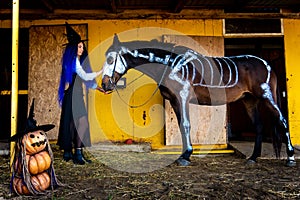 A girl dressed as a witch took a horse out of a corral with a skeleton painted in white paint