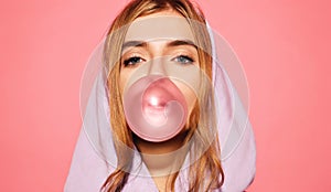 Girl dressed in blue hoodie and blowing bubble with chewing gum