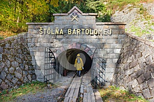 Dívka oblečená v hornické římse, s přilbou a lucernou vchází do důlní šachty Bartolomej