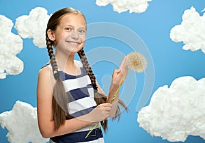 Girl dressed in striped dress posing on a blue background with cotton clouds, white air balloon, the concept of summer and happine