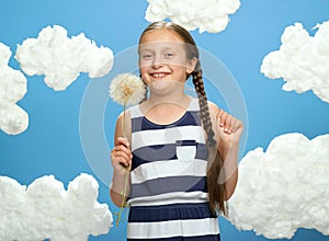 Girl dressed in striped dress posing on a blue background with cotton clouds, white air balloon, the concept of summer and happine