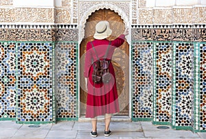 Girl dressing in red with hat looking the Ben Youssef Madrasa in marrakesh, morocco