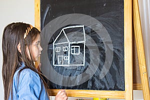 Girl drew a house and the sun with chalk on the Board