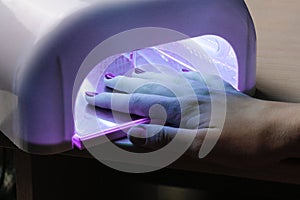 Girl dries gel polish applied to the nails under an ultraviolet lamp