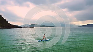 Girl drifts on paddleboard in pose Crescent Lunge Twist on Knee