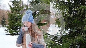 Girl drink hot tea in a thermos in snowy forest