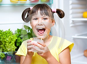 Girl drink milk standing near refrigerator