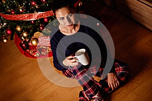 Girl drinking beverage in front of christmas tree