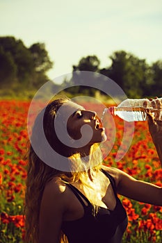 Girl drinking bottle of water in poppy field