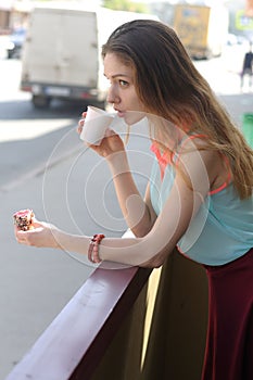 Girl is drinking coffee on a balcony near the road