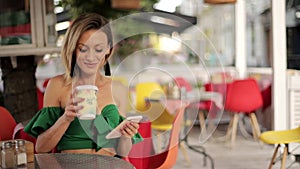 Girl drinking coffee in a cafe and talking on a smartphone, a happy woman