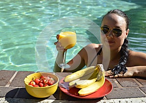 Girl drinking orange juice and eating fruits in the pool