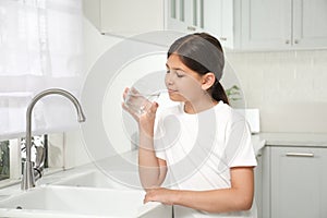 Girl drinking tap water from glass in kitchen