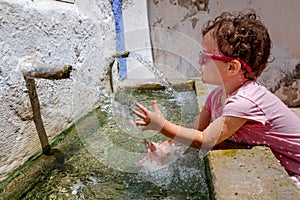 Girl drinking water from a fresh fountain in a mountain village