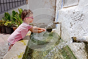 Girl drinking water from a fresh fountain in a mountain village