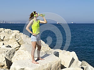 Girl drinking water on large rock by the seaside