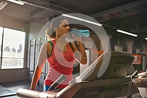 Girl drinking water while running on treadmill