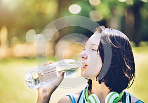 A girl drinking water with thirst after exercise, with a park in
