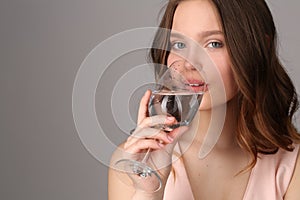 Girl drinking water from a wine glass. Close up. Gray background