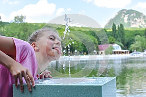 Girl drinks clean water from a fountain. drinking public fountain with water
