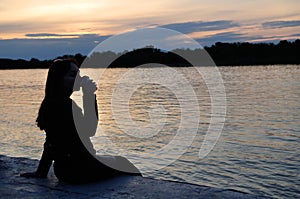 A girl drinks coffee sitting by the river at sunset