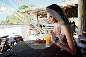 Girl drinks juice and checks the phone cafe on vacation with a view of the sea and the beach.