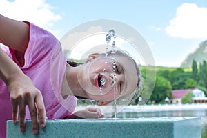 Girl drinks spring water from fountain. Drinking mineral water in fresh air.