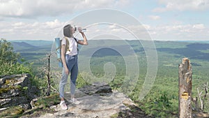 The girl drinks water on peak of the mountain after a long journey to the top.