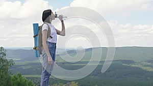 The girl drinks water on peak of the mountain after a long journey to the top.