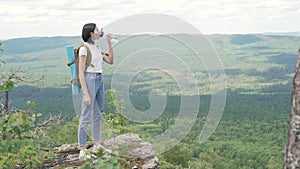 The girl drinks water on peak of the mountain after a long journey to the top.