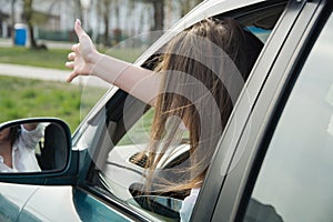 A girl drives a car and swears, shows her hand through the window to another driver or pedestrian. Woman driving