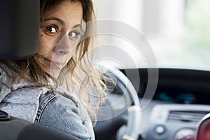 Girl driving car. Young woman behind driver`s seat looking at car`s rear seat.