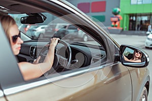 A girl driving a right-hand drive car is parked in a parking lot, near a shopping center, left-hand traffic. Close-up