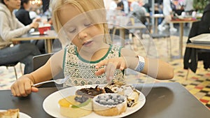 Girl eating assorted cakes in a cafe on a blurred background.