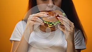 Girl eating burger, enjoying fast food, high calorie nutrition, risk of obesity