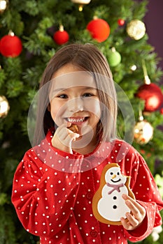 Girl Eating Cookie In Front Of Christmas Tree