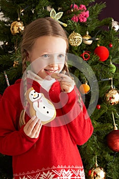Girl Eating Cookie In Front Of Christmas Tree