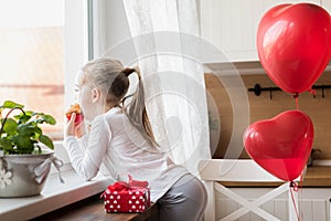 Girl eating her birthday cupcake in the kitchen, surrounded by balloons.