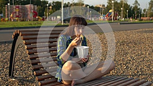 Girl eating hot noodles on the pebble beach of the river bank.