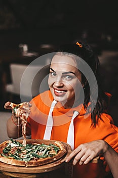 girl eating pizza. a girl in an orange sweater eats pizza appetizingly. stretching cheese, tasty, juicy.