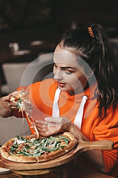 girl eating pizza. a girl in an orange sweater eats pizza appetizingly. stretching cheese, tasty, juicy.