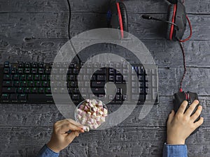 Girl eating a red and white marshmallow sitting at the gaming computer keyboard.