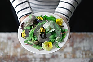 Girl is eating salad.Beautiful mix of salads with flowers on a white plate. Diet concept. Nutrition for girls. Healthy vegan food.