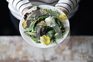 Girl is eating salad.Beautiful mix of salads with flowers on a white plate. Diet concept. Nutrition for girls. Healthy vegan food.