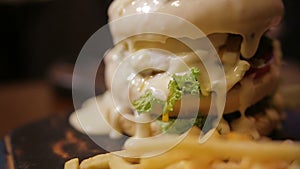 Girl eating at the table french fries burger with veal lettuce vegetables burger poured with cheese sauce on top