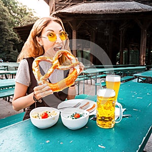 Girl eating traditional Pretzel and drinking fresh Bavarian beer in beer garden in Munich. The concept of traditional food