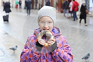 The girl eats a bagel with poppy on a city street, cold day.